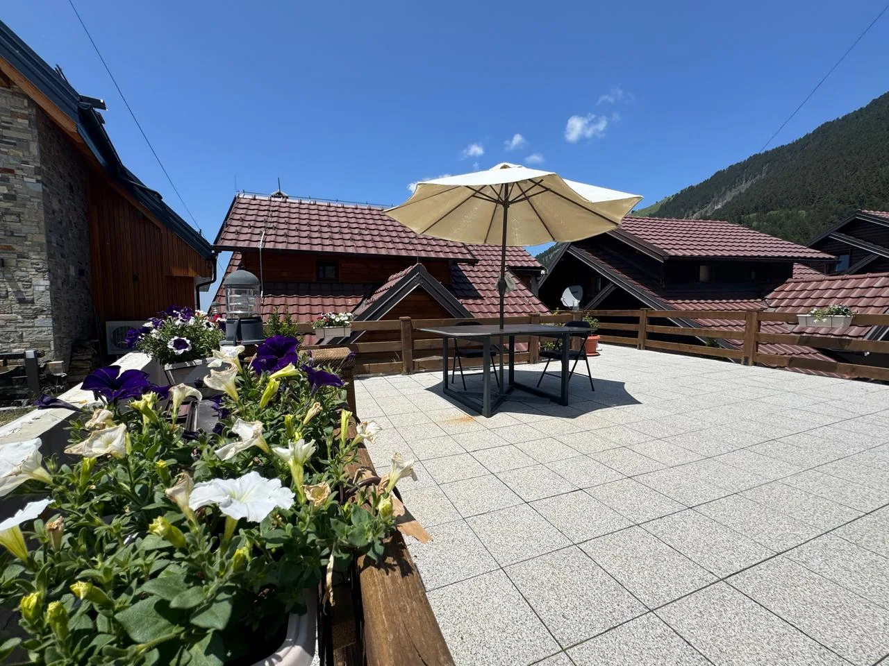 Sunny terrace at Villa Bjeshka in Prevallë with flowers, parasol and mountains behind